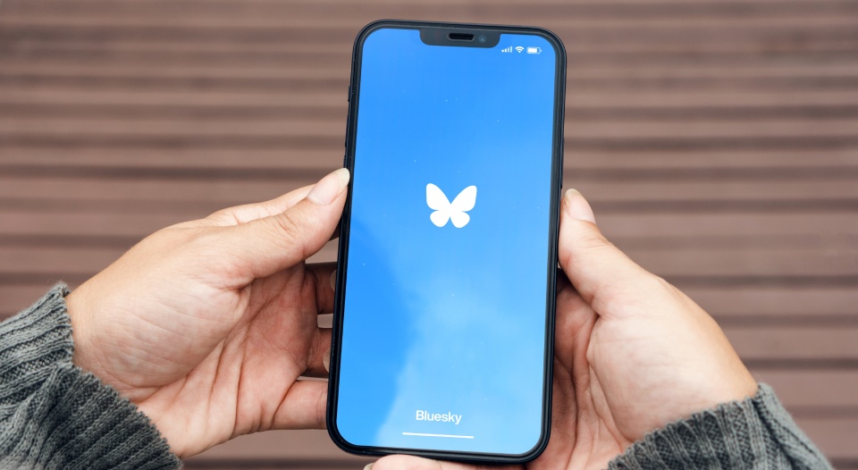 Girl in the park holding a smartphone with Bluesky social media app on the screen. Wooden bridge, green area and an artificial lake. Rio de Janeiro, RJ, Brazil. September 11 2024.